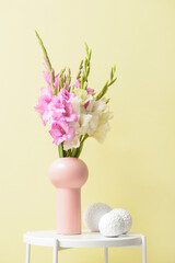 Vase with beautiful gladiolus flowers and decor on table near color wall