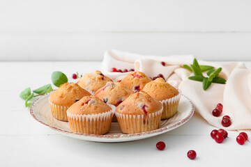 Plate with tasty cranberry muffins on light wooden background