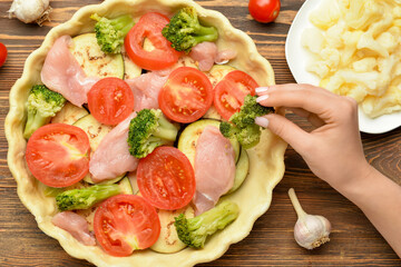Woman preparing chicken pot pie with vegetables on wooden background