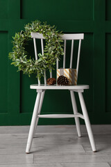 Christmas mistletoe wreath and gift on chair near color wall