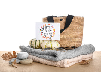 Towels, bag, pumpkins, stones and card with text HAPPY THANKSGIVING on beige table against white background