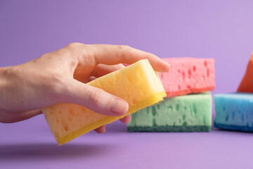 Hand holding yellow sponge on purple background. Ready for dish wash. Kitchen cleaning sponges