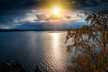 Beautiful lake and rocky shore in the rays of evening sun of golden autumn in cloudy weather