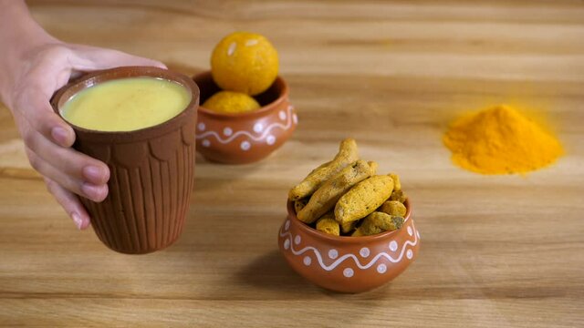 Chilled haldi milk served in an earthenware glass - Golden milk. Indian traditional sweet / Laddus  Namkeen  and powdered Haldi kept together - evening snacks  tasty food  homemade  medicinal herb
