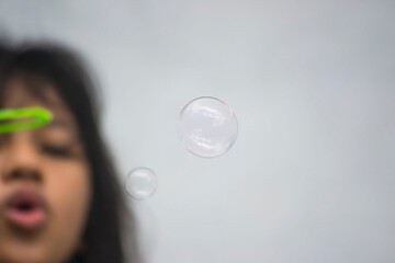 A girl holding a bubble maker and blowing them out.  Image focused on the bubble.