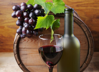 A glass of red wine, a bottle, a barrel of wine and a bunch of grapes.
