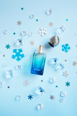 Open perfume bottle with snowflakes, ice cubes, small hearts on the blue background. New year,...