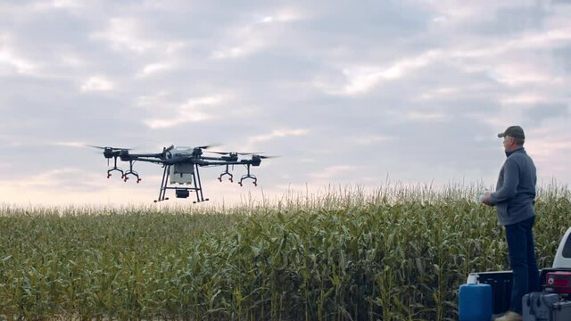 Farmer is landing his huge intelligent agriculture drone with spray nozzles near corn field early in the morning