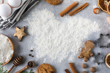 Obraz na płótnie Canvas Christmas background with flour on a gray background surrounded by spices, rolling pin and cookies.