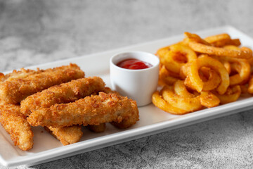 Chicken goujons, coated in breadcrumbs, with spicy curly fries and a tomato ketchup dip on a white...