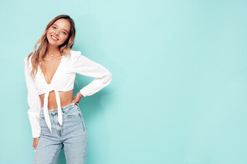 Portrait of young beautiful smiling female in trendy summer clothes. Sexy carefree woman posing near blue wall in studio. Positive model having fun indoors. Cheerful and happy
