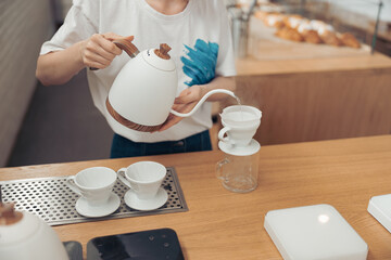 Fototapeta na wymiar Female barista pouring boiled water through filter into glass mug