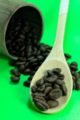 Coffee beans on a bamboo spoon. There is coffee scattered with a green background