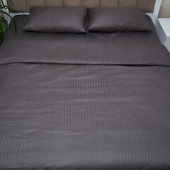 A large bed with a brown-gray bedding(linens)  are in the bedroom. 