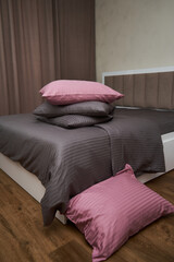 A large bed with a brown-gray bedding(linens) and pink pillows are in the bedroom.