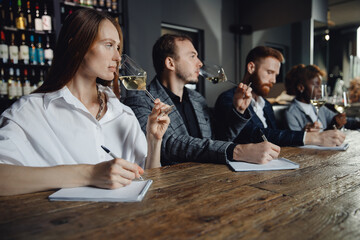 Sommeliers female and male tasting white wine and making notes at degustation card notepad