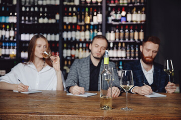 Sommeliers female and male tasting white wine and making notes at degustation card notepad