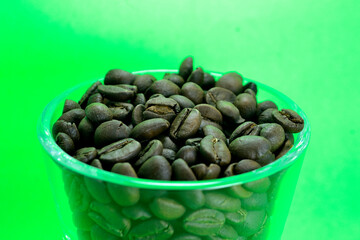 Coffee beans in a transparent glass on a clean green background
