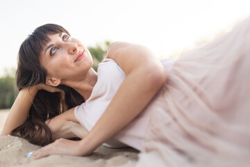 a girl in a pink dress lies on the sand