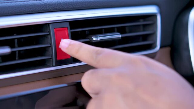 Closeup of driver's hand pushing car hazard emergency lights button after breakdown accident on the road. 