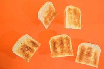 Flying roasted pieces of bread on orange pastel background. Fresh roasted pieces of toasts on orange background
