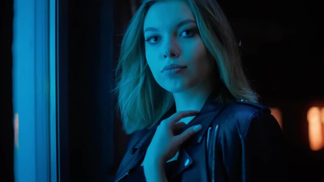 Close-up portrait of charming blonde girl standing in the blue neon light of a vending machine. Her hair is blowing in the wind. Photo shoot for a fashion magazine.