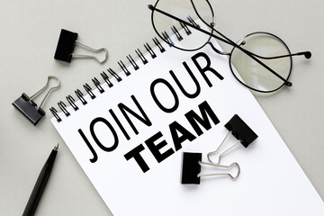JOIN OUR TEAM. Notepad on gray background surrounded glasses pencils
