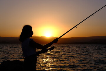 silhouette of woman fishing at sunset.