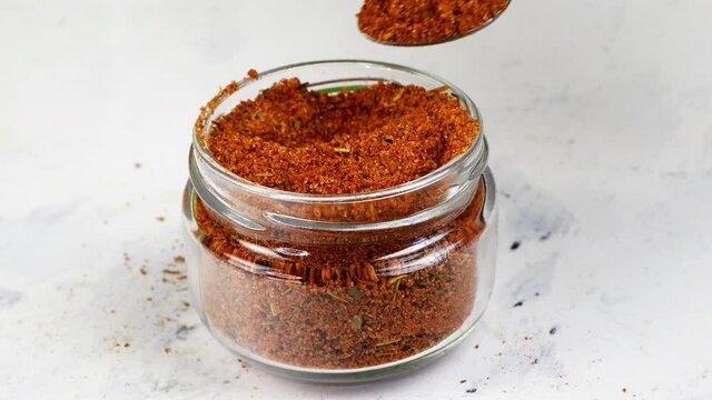 Chef taking with teaspoon spices ground red pepper or chili from glass spice jar.