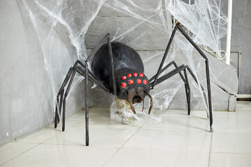 A large not real black spider stands in the corner near the web, as a decoration decoration
