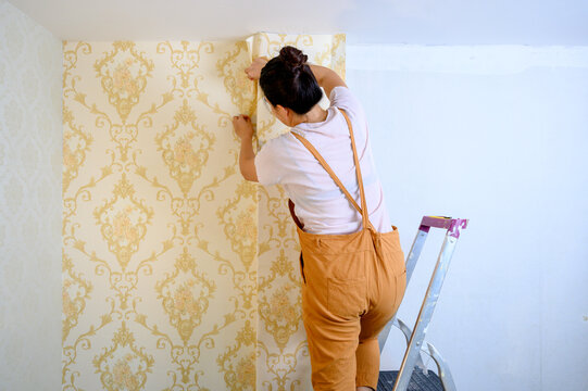 Asian woman applying new wallpaper at home. Renovate and house decoration.