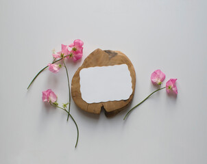 A mockup of an empty white sheet of paper for postcards and an invitation card on a wooden stand, pink sweet pea flowers on a light table background.