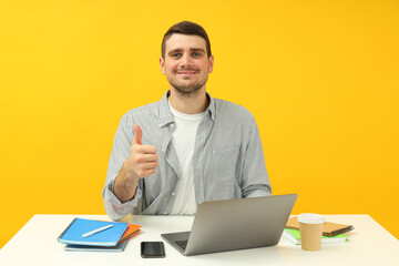 Study concept with young man sitting on the table on yellow background