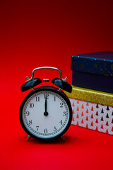 Time for New Year and Christmas gifts. A black vintage alarm clock and gift boxes in the background are isolated on a red background. It's holiday time.