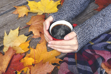 Autumn drink tea or coffee in hands on the background of October yellow leaves. Autumn comfort and mood background concept.