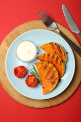 Concept of tasty food with baked pumpkin on red background