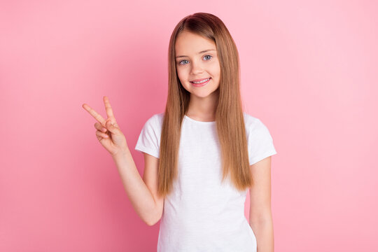 Photo of cool blond little girl show v-sign wear white t-shirt isolated on pink color background
