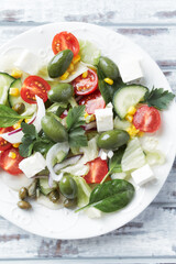 Healthy Salad with Feta Cheese, Green Olives, Baby Spinach, Cucumber, Cherry Tomatoes and Capers. Bright wooden background. Top view. Close up. 