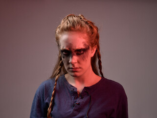 Closeup portrait of young red haired woman with black barbarian facepaint wearing medieval viking inspired costume Holding  sheep skull for ritual  posing against studio background with red lighting