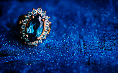 Closeup of luxury wedding ring in dark blue glitter background. Bridal golden jewelry gift with precious gemstone.