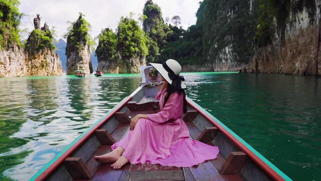Beautiful girl sitting on the boat and looking to mountains in Ratchaprapha Dam at Khao Sok National Park, Surat Thani Province, Thailand.