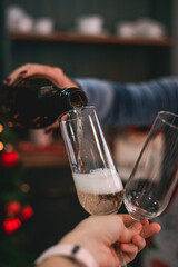 A hand pours champagne from a bottle into glasses on the background of a Christmas tree
