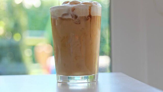 Ice Coffee preparation, pouring syrup in coffee with milk and ice cubes Coffee break. Iced coffee at home.