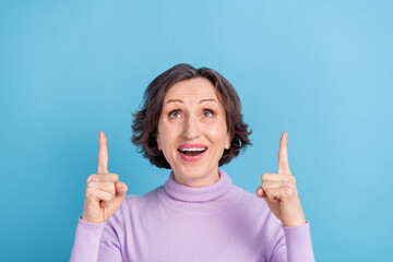 Photo of excited mature woman happy positive smile indicate fingers empty space select suggest isolated over blue color background