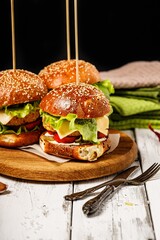 Appetizing homemade chicken burger with cheese, fresh salad and vegetables on a round cutting board. Lettuce leaves, tomatoes and onions. Traditional American fast food. Rustic background. Copy space