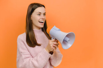 Fun expressive happy smiling student caucasian female 20s scream aside shouting in megaphone, dressed in pink knitted sweater, isolated on orange color background studio. People lifestyle concept
