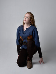 Full length portrait of red haired woman wearing medieval viking inspired costume,  Holding a long sword weapon, sitting pose against studio background.