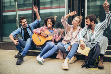Group of young people hangout in city.They are sitting,singing and playing guitar.