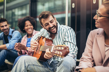 Group of young people hangout in city.They are sitting,singing and playing guitar.