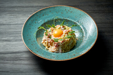 Appetizing italian pasta carbonara with yolk, white sauce and bacon in a blue plate on a wooden background